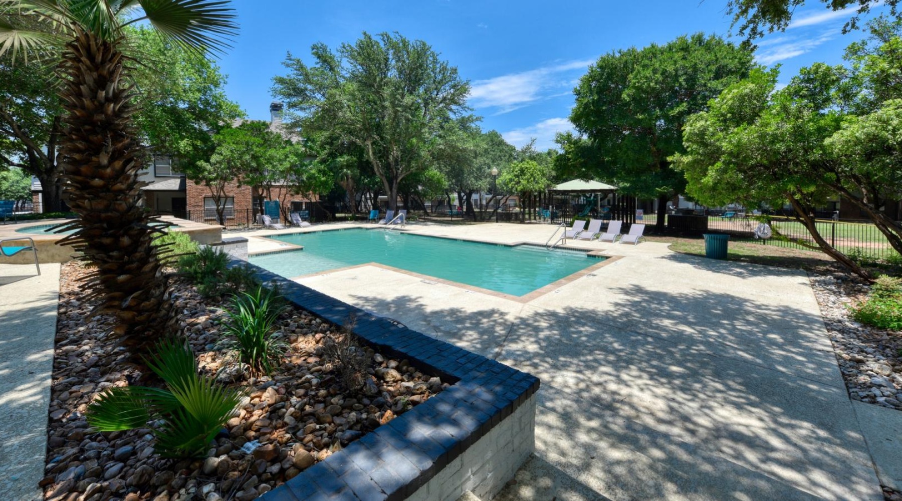 Relax and unwind poolside a pool with trees and a building in the background